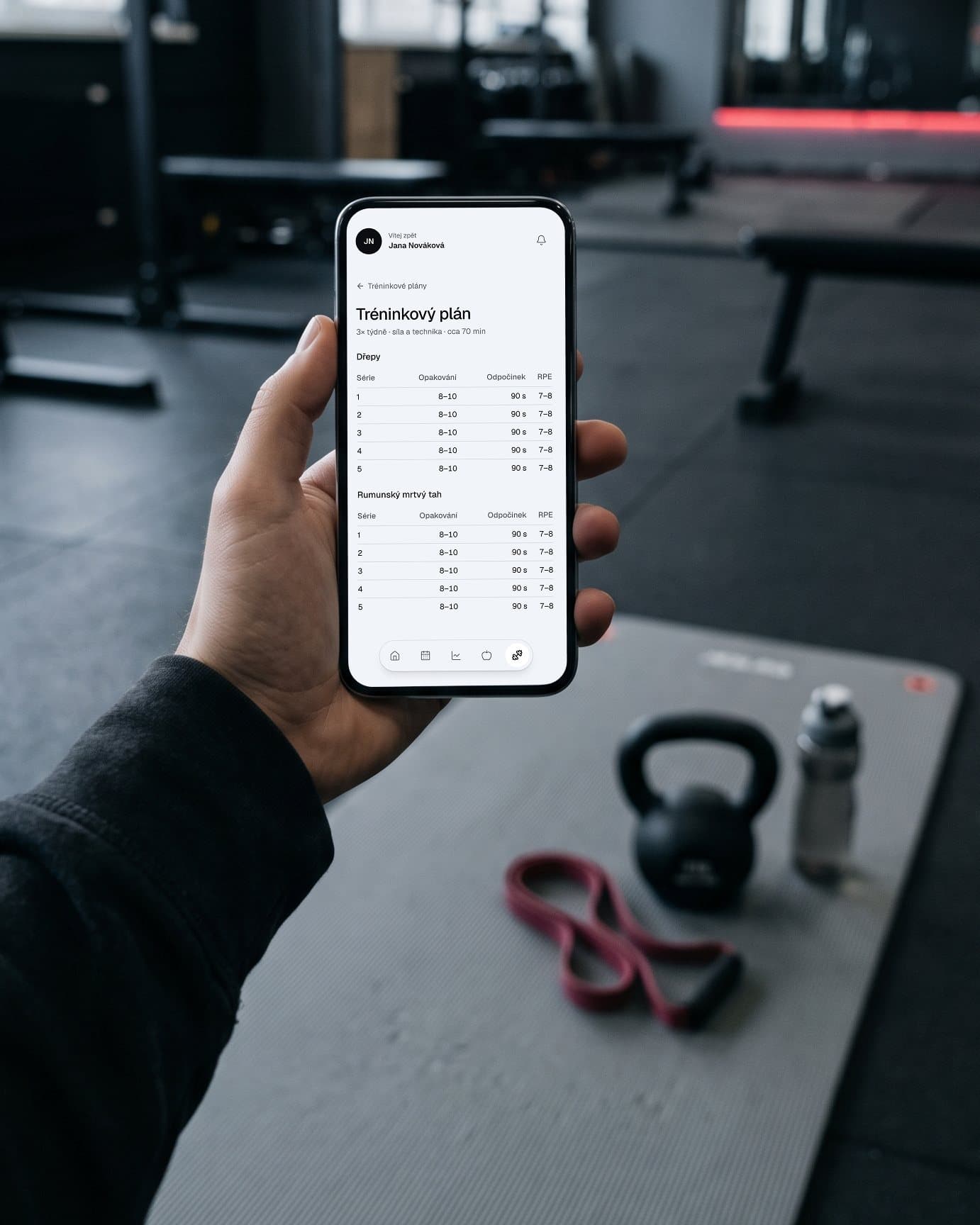 Tréninkový plán v klientské zóně v telefonu, v posilovně nad podložkou s kettlebellem